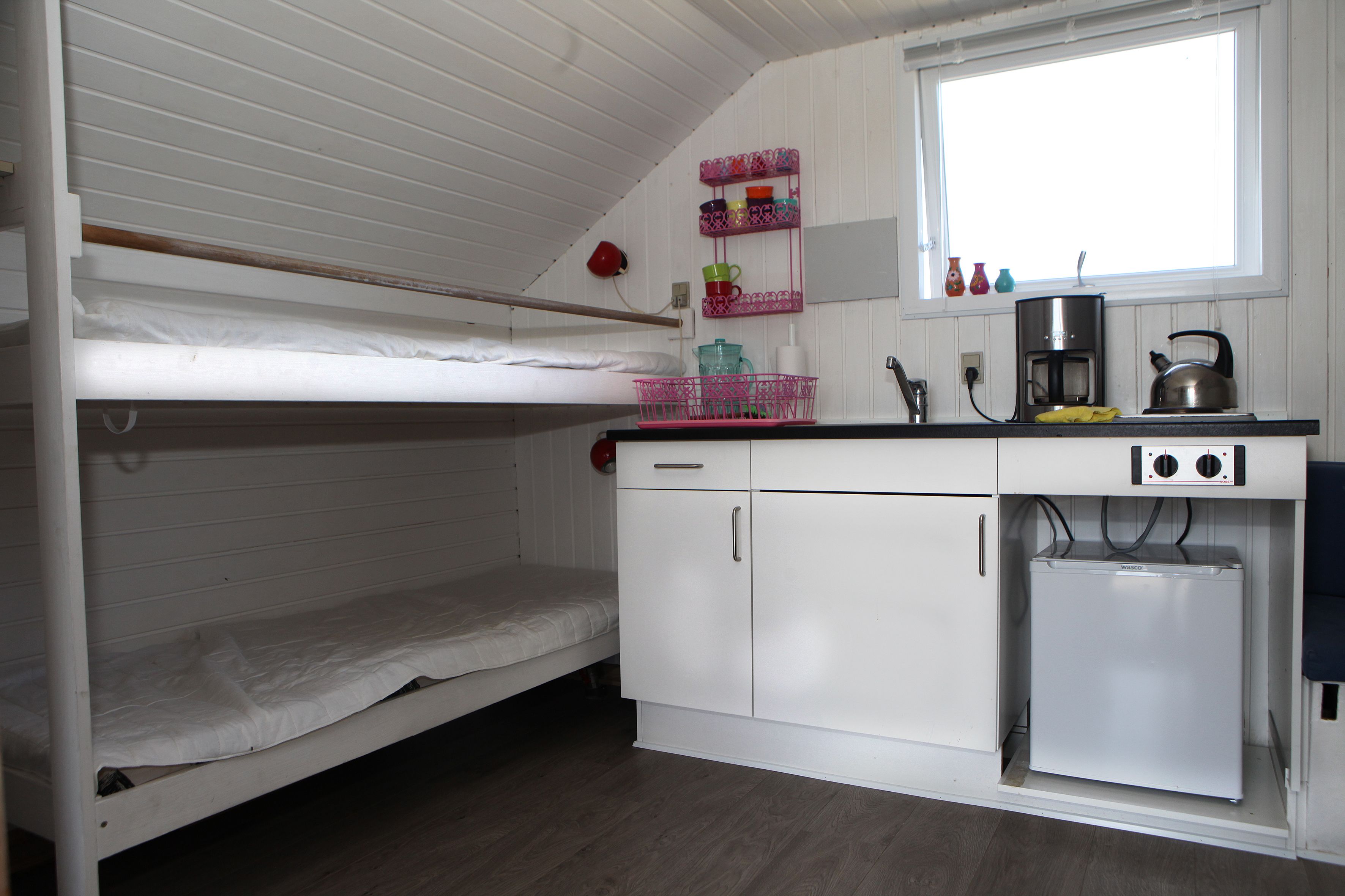 A compact room with bunk beds, a kitchenette with a refrigerator, and a window.