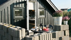 Ein gemütliches Holzhaus mit kleinem Balkon, einem Tisch mit Laterne und Topfpflanzen.