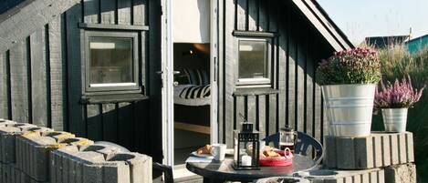 A cozy wooden cabin with a small balcony, a table with a lantern, and potted plants.