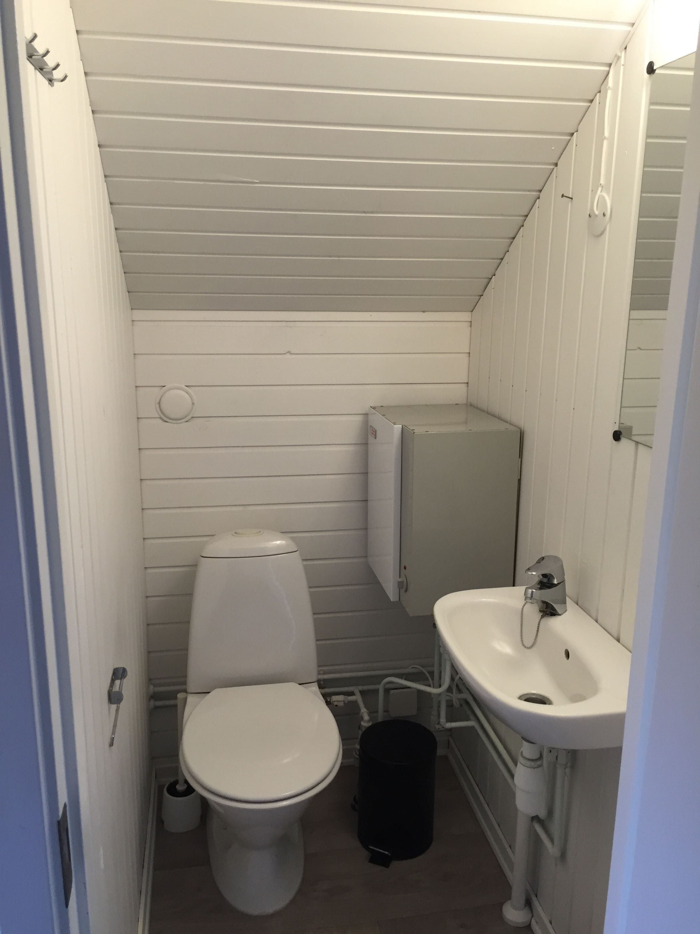 A small, compact bathroom with a toilet, sink, and a storage cabinet.