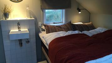 A bedroom with a bed, a window, a bedside lamp, a sink, and a mirror.