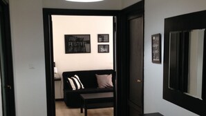 A hallway with a black door, a black bench, and a black sofa with a white pillow. There are three framed signs on the wall. - Iron Bridge Accomodation (Rome)