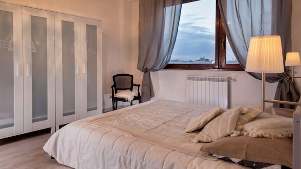A bedroom with a large bed, a chair, a wardrobe, and a window with curtains. - Iron Bridge Accomodation (Rome)