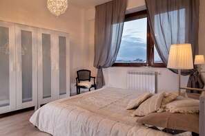 A bedroom with a large bed, a chair, a wardrobe, and a window with curtains. - Iron Bridge Accomodation (Rome)