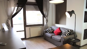 A modern living room with a grey sofa, black and white patterned pillows, a red accent pillow, a small black side table, and a floor lamp. - Iron Bridge Accomodation (Rome)