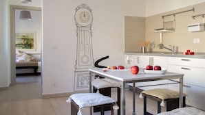 A modern kitchen with a white countertop, a clock mural, and a dining area with a table and chairs. - Iron Bridge Accomodation (Rome)