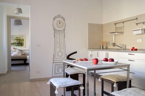 Eine moderne Küche mit weißer Arbeitsplatte, einer Wandmalerei mit einer Uhr und einem Essbereich inklusive Tisch und Stühlen.