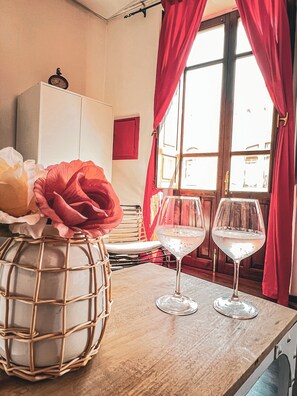 A room with a wooden table, two wine glasses, a decorative vase with flowers, and a clock on the wall.