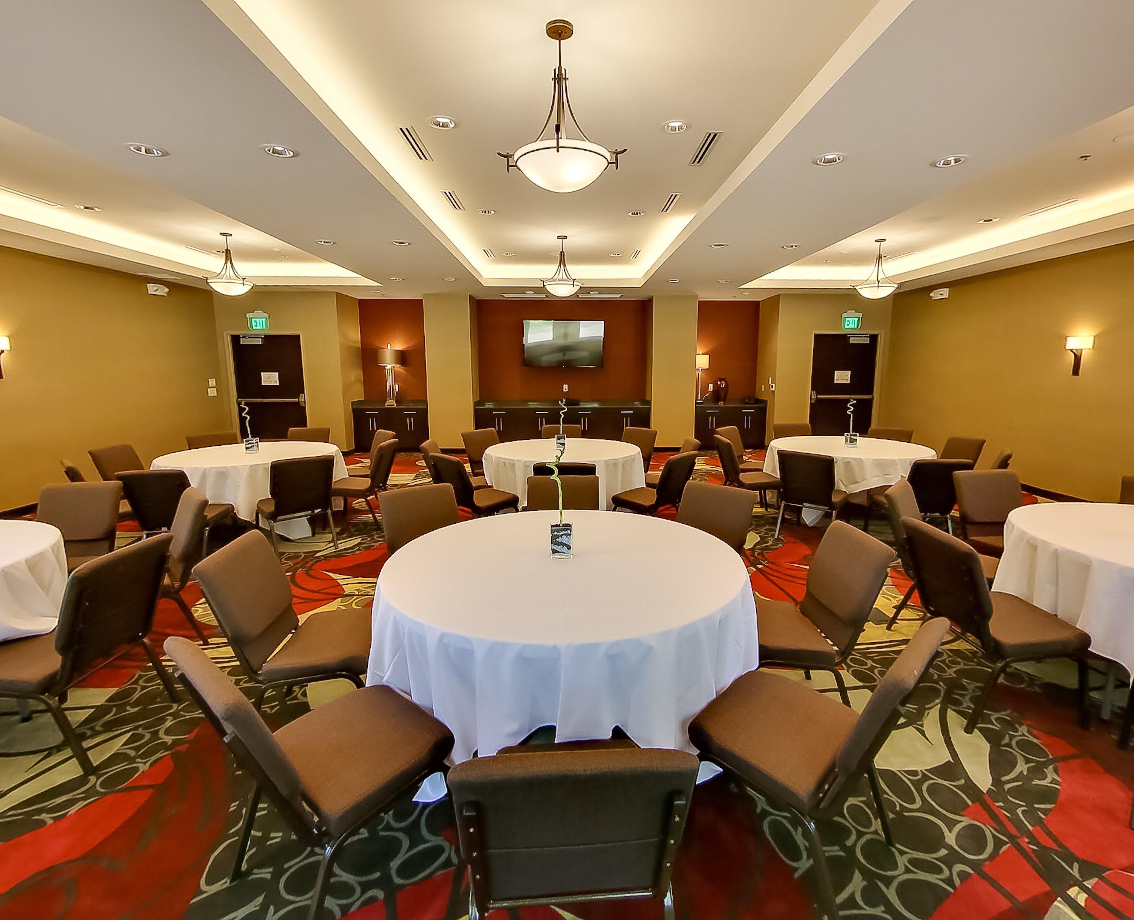 Een hotelconferentiezaal met meerdere ronde tafels, stoelen, een flatscreen televisie en een vloerbedekking.