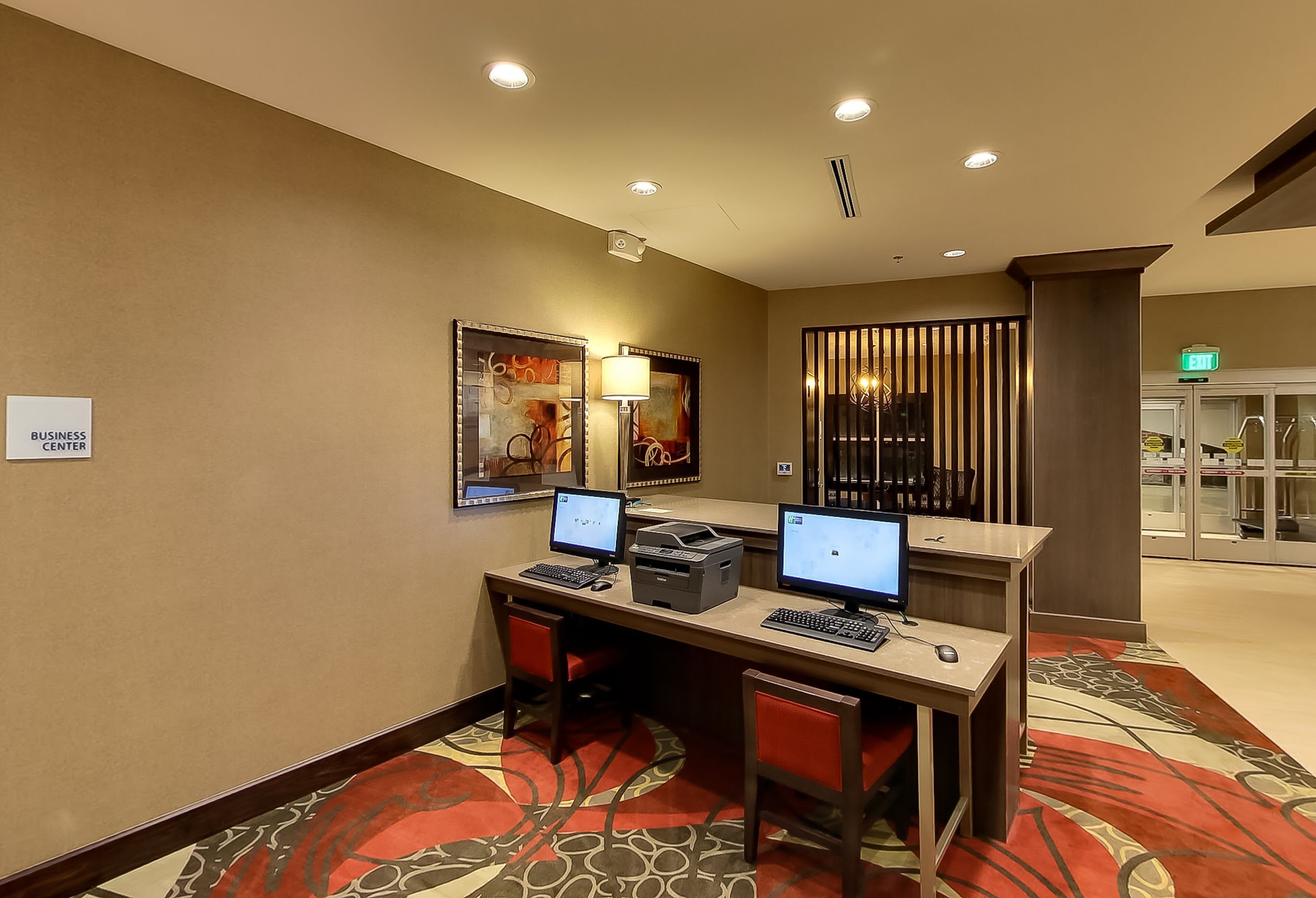 Un centre d’affaires équipé de deux postes de travail informatiques, d’une imprimante et d’une lampe fixée au mur.