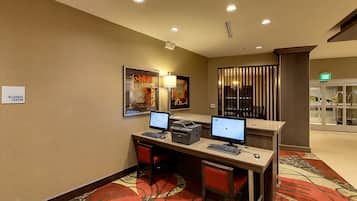 Un centre d’affaires équipé de deux postes de travail informatiques, d’une imprimante et d’une lampe fixée au mur.