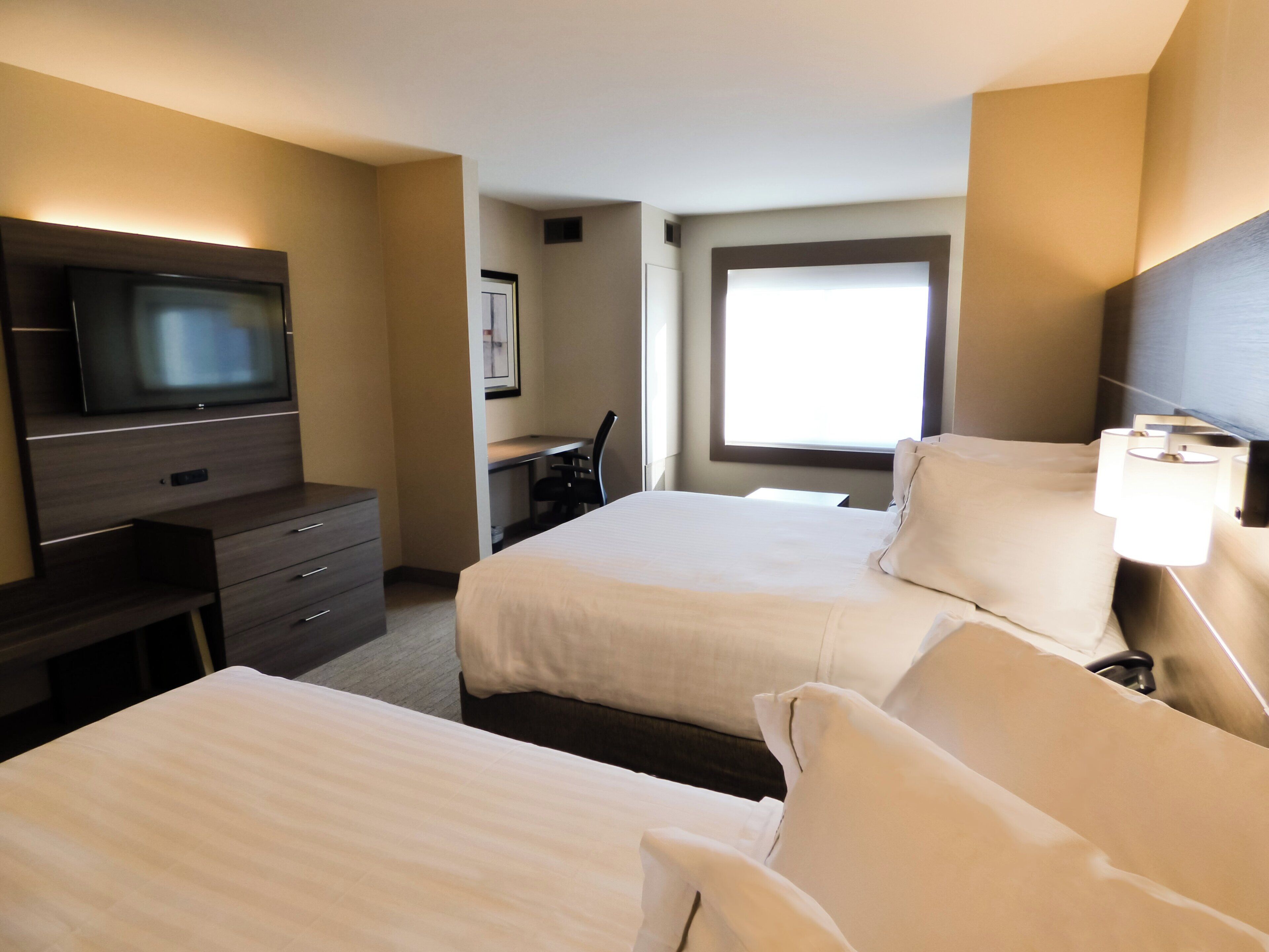 Een hotelkamer met twee bedden, een bureau, een televisie en een raam.