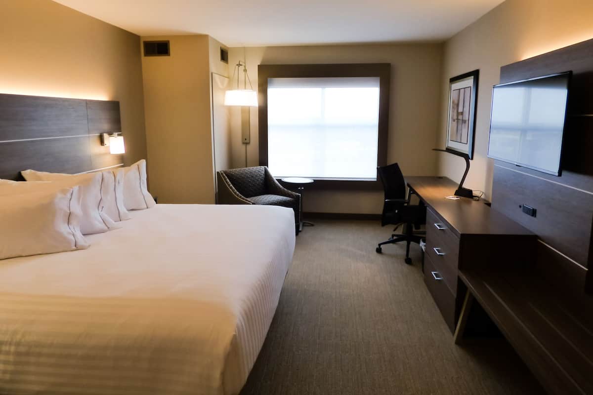 A hotel room with a large bed, a desk with a chair, a television, and a window with natural light.
