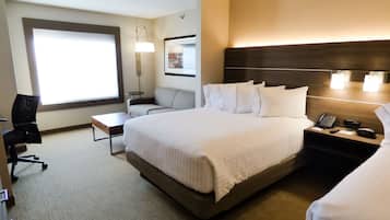 A hotel room with a large bed, a desk, a chair, a nightstand with a phone, and a window with blinds.