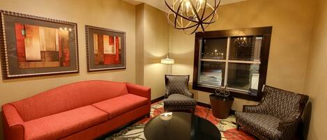 A hotel room with a red sofa, patterned armchairs, a round table, and artwork on the walls.