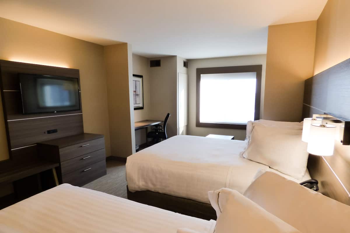 A hotel room with two beds, a desk, a television, and a window.