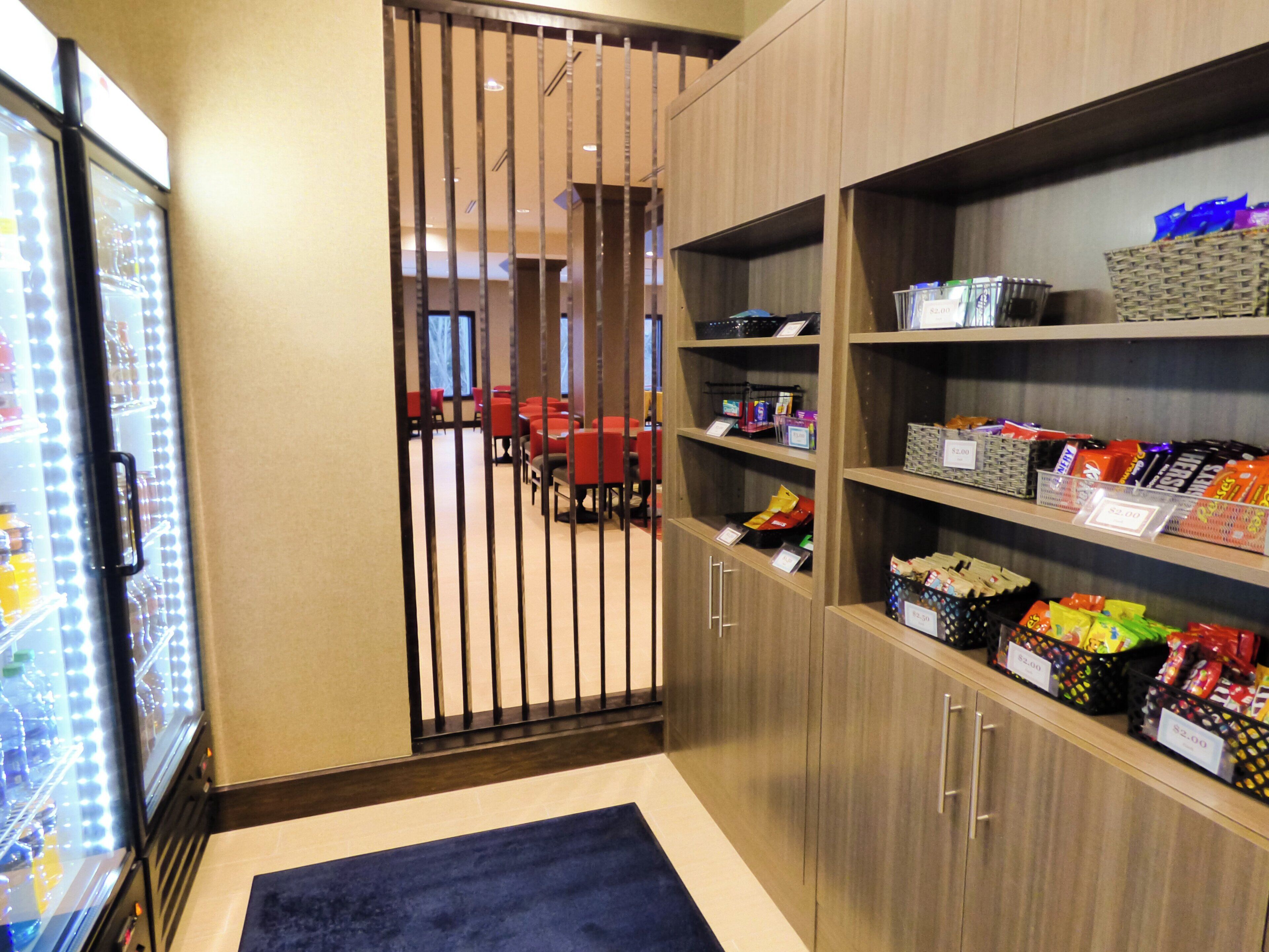 A hotel room with a minibar, a seating area with red chairs, and shelves stocked with snacks.