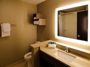 Un baño con inodoro, lavabo y espejo. Hay toallas y artículos de aseo en la encimera.
