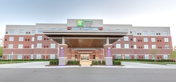 Un hotel Holiday Inn Express con fachada de ladrillo, entrada cubierta y jardín delantero ajardinado.
