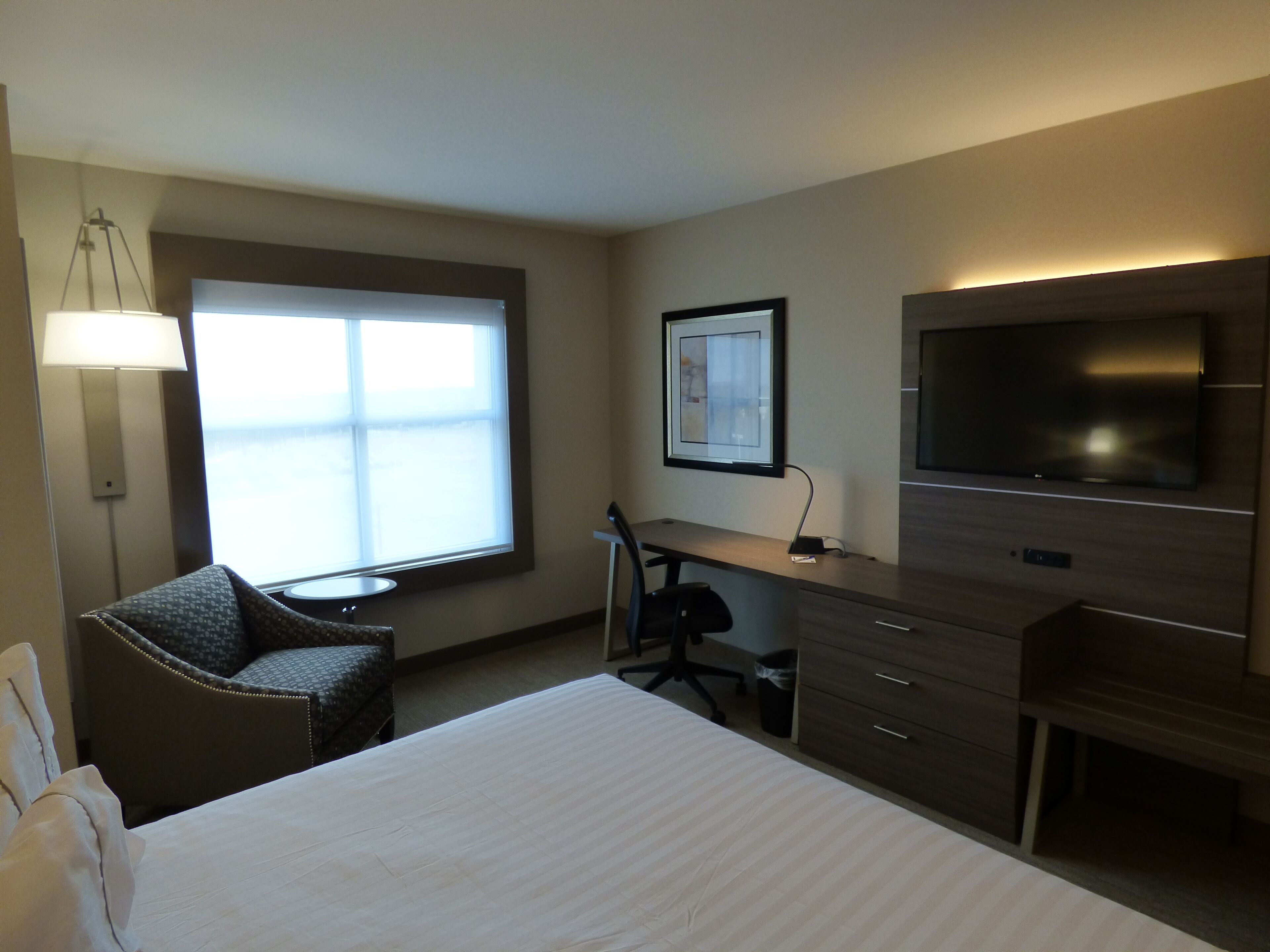 Une chambre d’hôtel équipée d’un lit, d’un bureau, d’une chaise, d’une télévision et d’une fenêtre avec des stores.