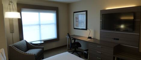 Une chambre d’hôtel équipée d’un lit, d’un bureau, d’une chaise, d’une télévision et d’une fenêtre avec des stores.
