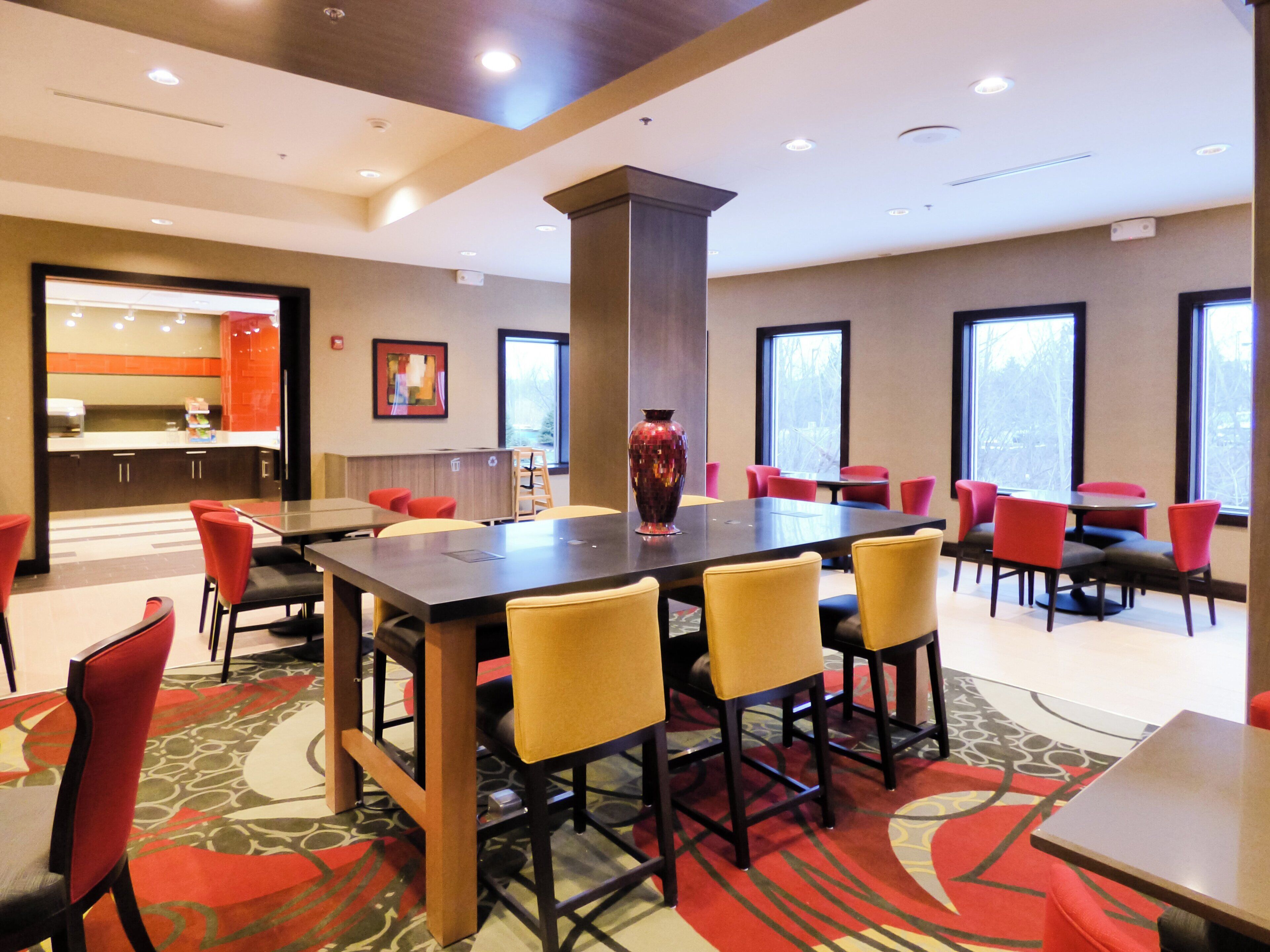 A conference room with a large table, red and yellow chairs, and a vase on the table.