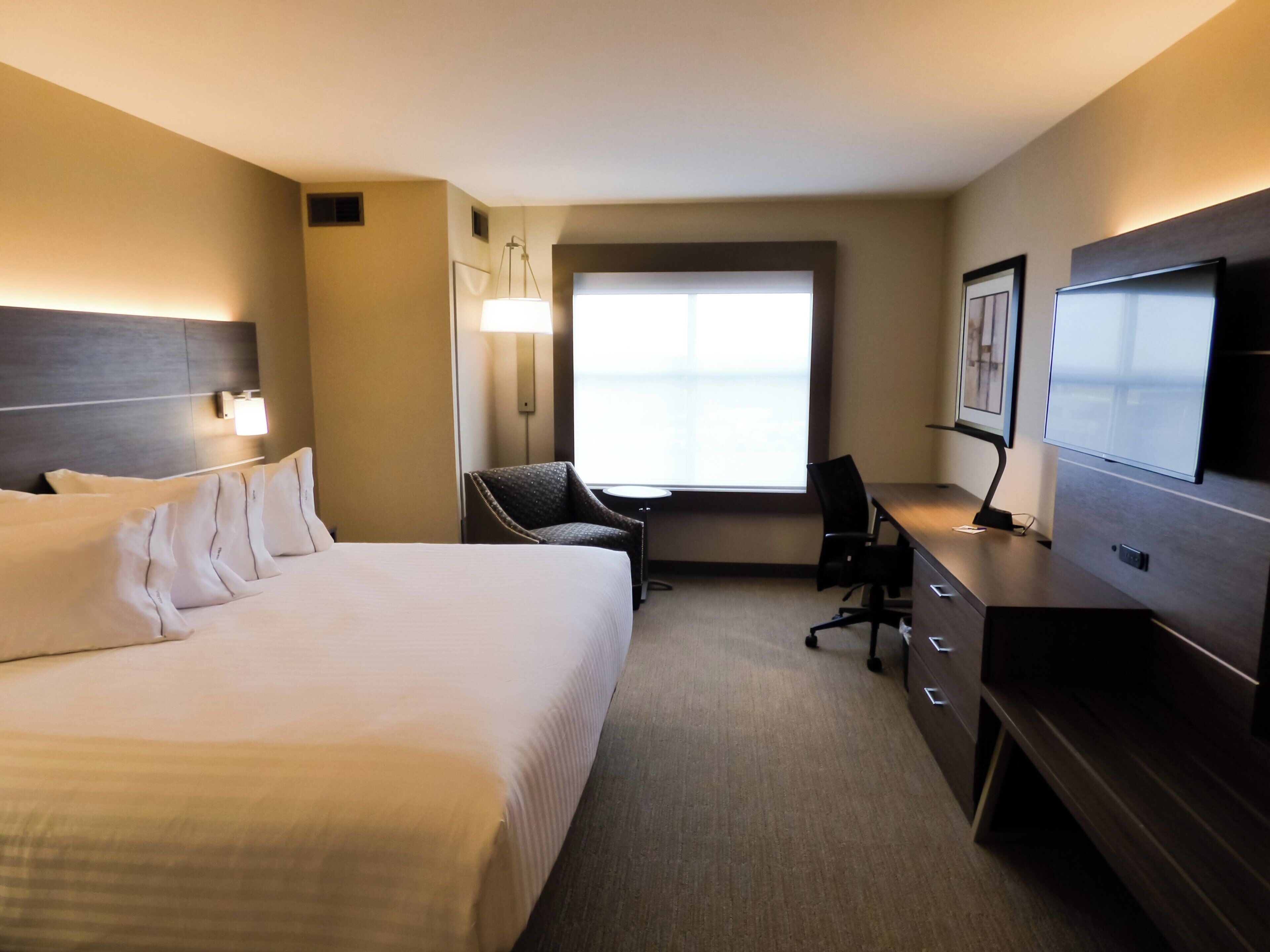 A hotel room with a large bed, a desk, a chair, a television, and a window.