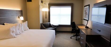 A hotel room with a large bed, a desk, a chair, a television, and a window.
