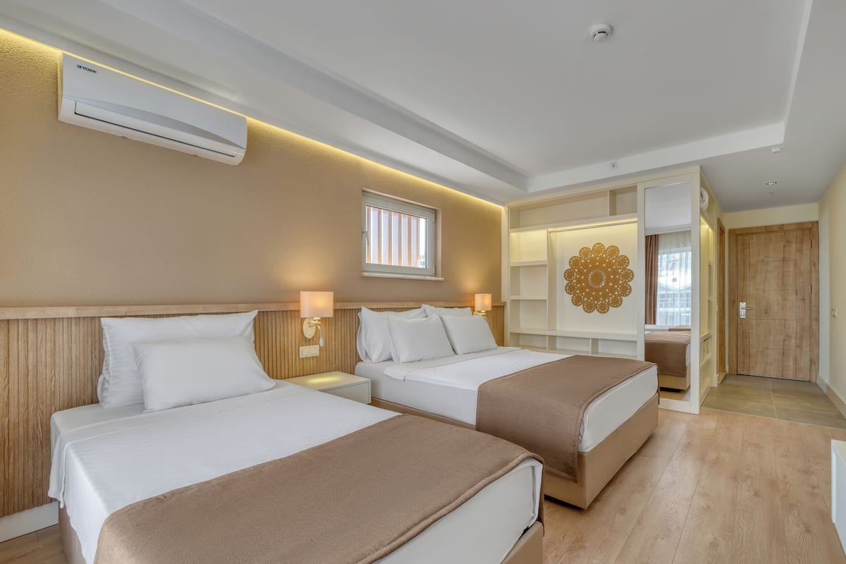 Habitación de hotel con dos camas, aire acondicionado de pared, un adorno en la pared y una puerta de madera.