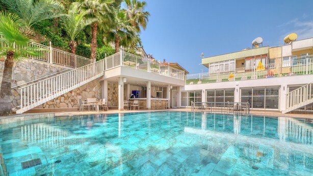 A clear blue pool with a stone border, a white railing, and a bar area with chairs and umbrellas. - Park Hotel (Alanya)