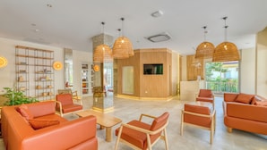 A modern hotel lobby with orange sofas, wooden chairs, a bookshelf, and a TV mounted on the wall. - Park Hotel (Alanya)