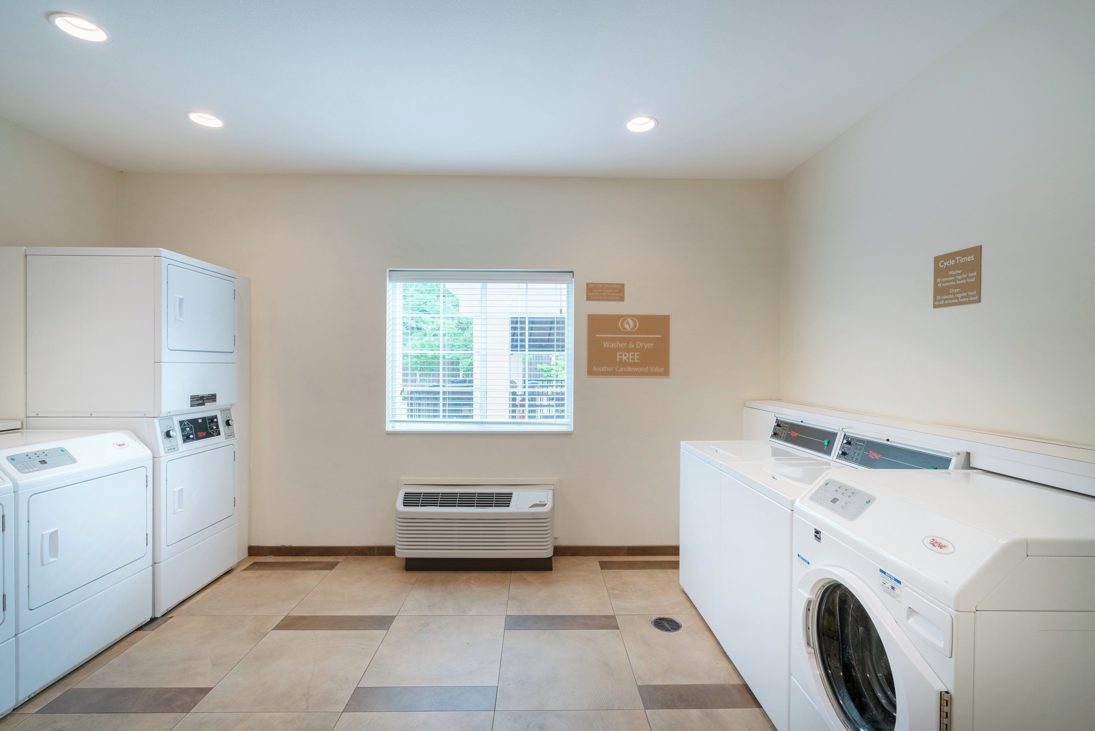 A laundry room with two washing machines, a dryer, and a vent unit. There are signs indicating cycle times for the washer and dryer.