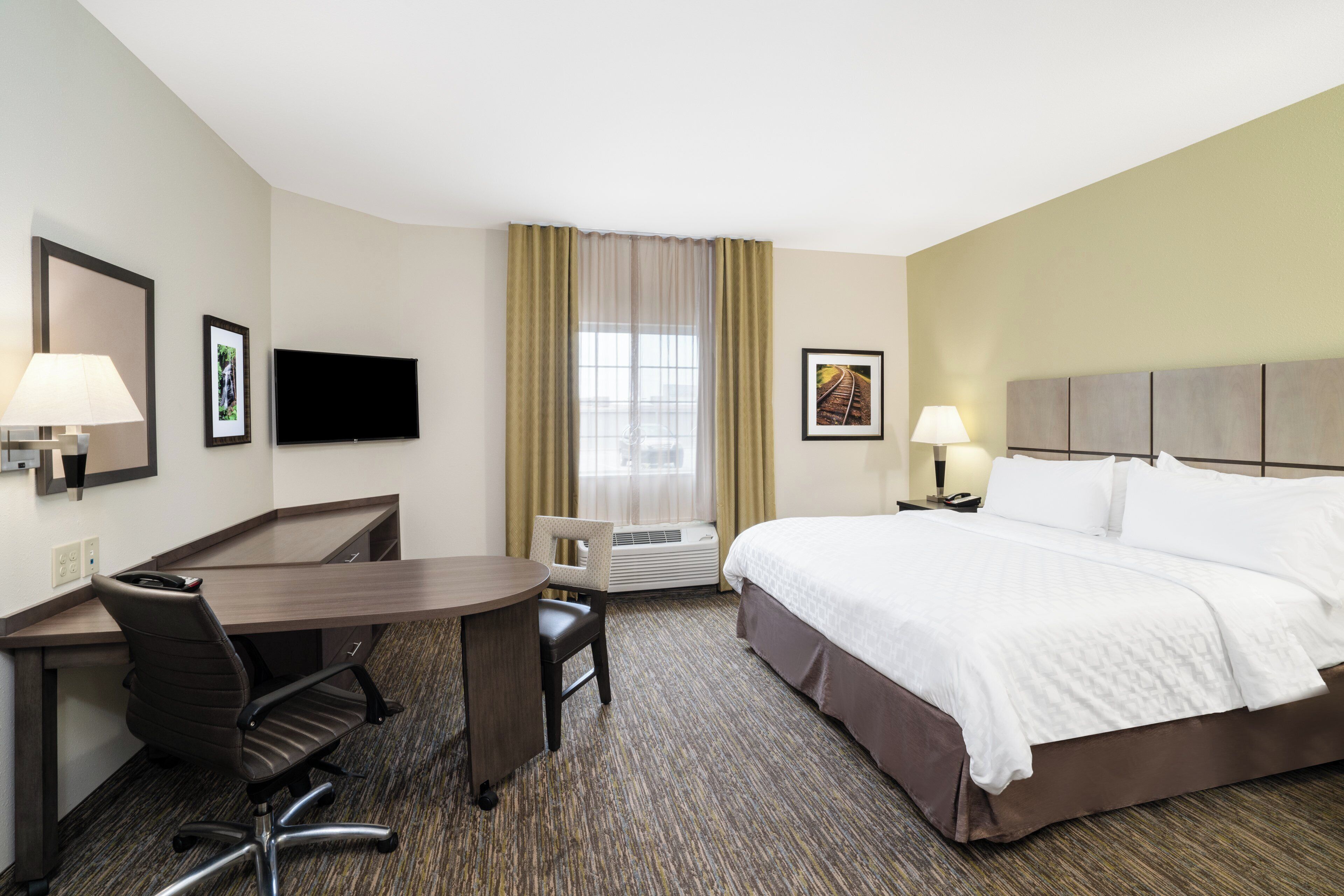 A hotel room with a bed, desk, chair, television, and a window with curtains.