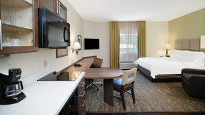 Habitación de hotel con cama, escritorio, silla, televisor, cafetera y unidad de aire acondicionado.