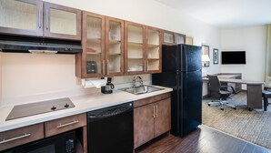 Una cocina compacta con armarios de madera, un refrigerador negro, lavavajillas y cafetera.