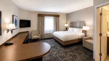 Une chambre d’hôtel comprenant un lit, deux tables de chevet avec des lampes, un bureau, une chaise, une télévision et une fenêtre avec des rideaux.