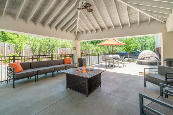 An outdoor patio with a fire pit, seating, and a covered area.