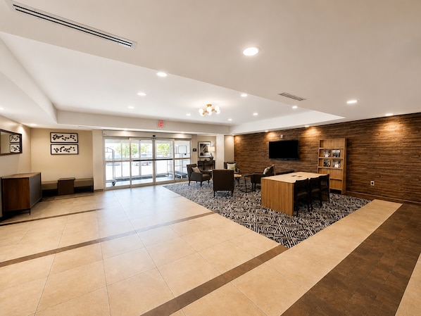 A hotel lobby with a reception desk, seating area, and a large window with a view of parked cars.