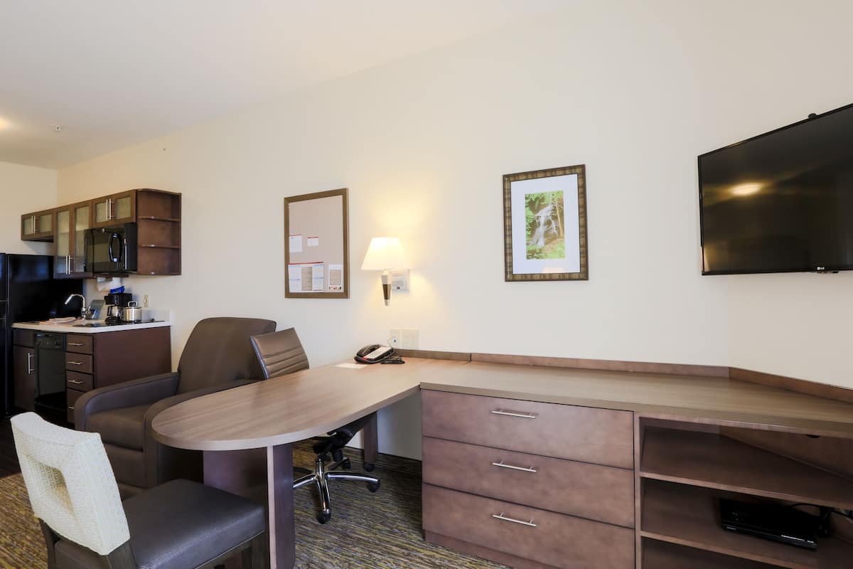 Een hotelkamer met een bureau, stoel, kitchenette en een flatscreen televisie.