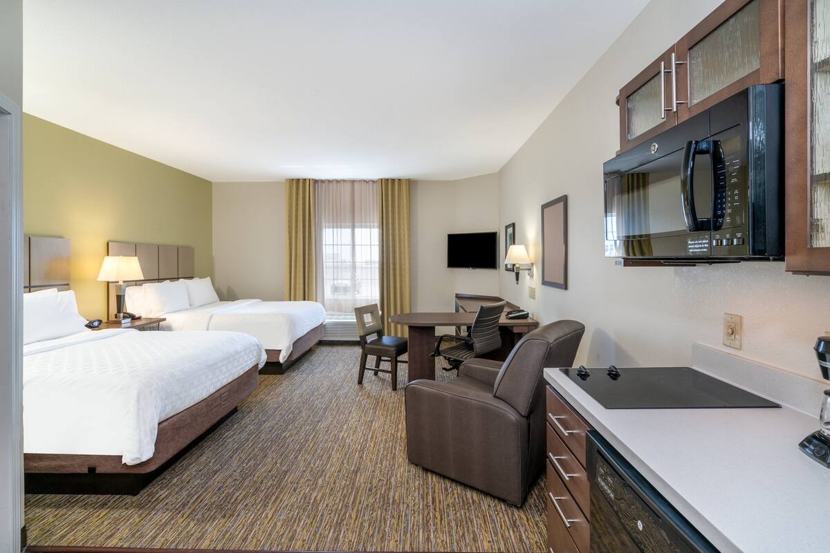 A hotel room with two beds, a desk, a chair, a microwave, and a television.