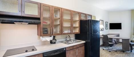 A modern kitchen with wooden cabinets, a black refrigerator, a coffee maker, and a dining area with a table and chairs.