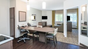 Habitación de hotel con una gran mesa de madera, dos sillas, un sofá, un televisor y un minibar.