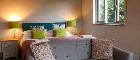 A bedroom with a bed, two bedside tables, a window, and a grey sofa.