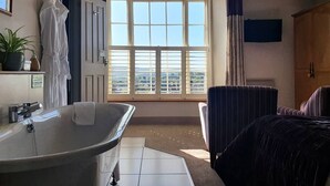 A room with a large window, a bathtub, a bed, and a chair. - The Castle Hotel (Bishops Castle)