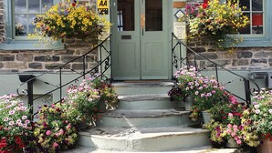 A stone building with a green door, two windows with flower boxes, and a sign indicating a restaurant. - The Castle Hotel (Bishops Castle)