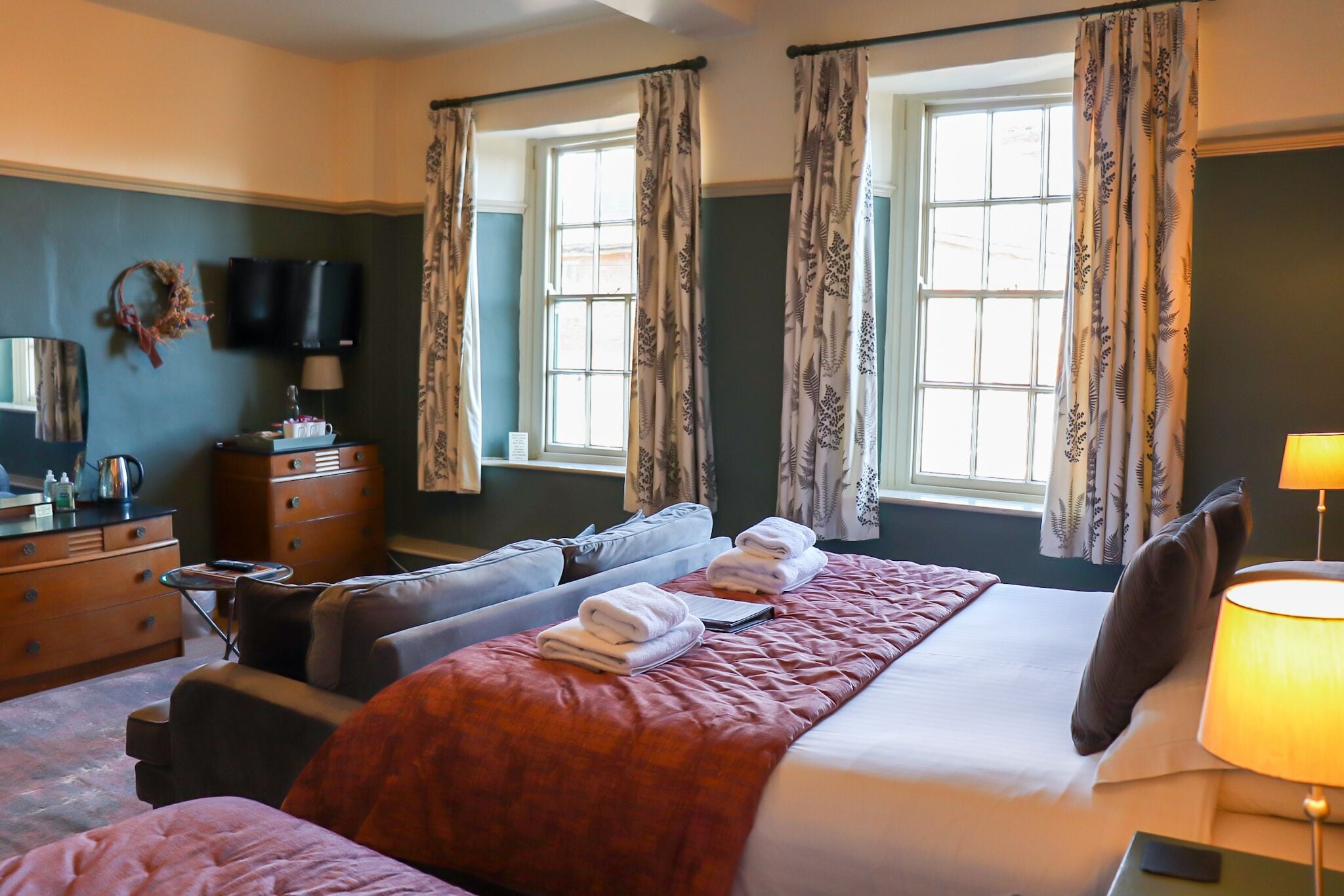 A hotel room with a large bed, two sofas, a dresser, a television, and a window with curtains.