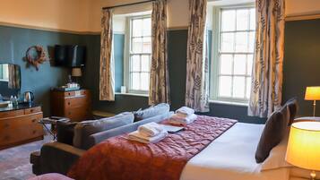 A hotel room with a large bed, two sofas, a dresser, a television, and a window with curtains.