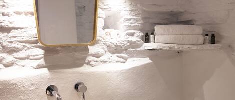 A bathroom with a round sink, a mirror with a gold frame, and a shelf with towels and toiletries.