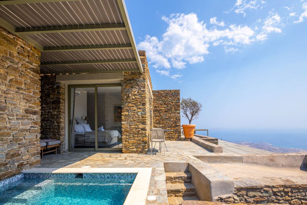 A stone building with a pool, a bedroom with a sliding door, and a view of the sea.