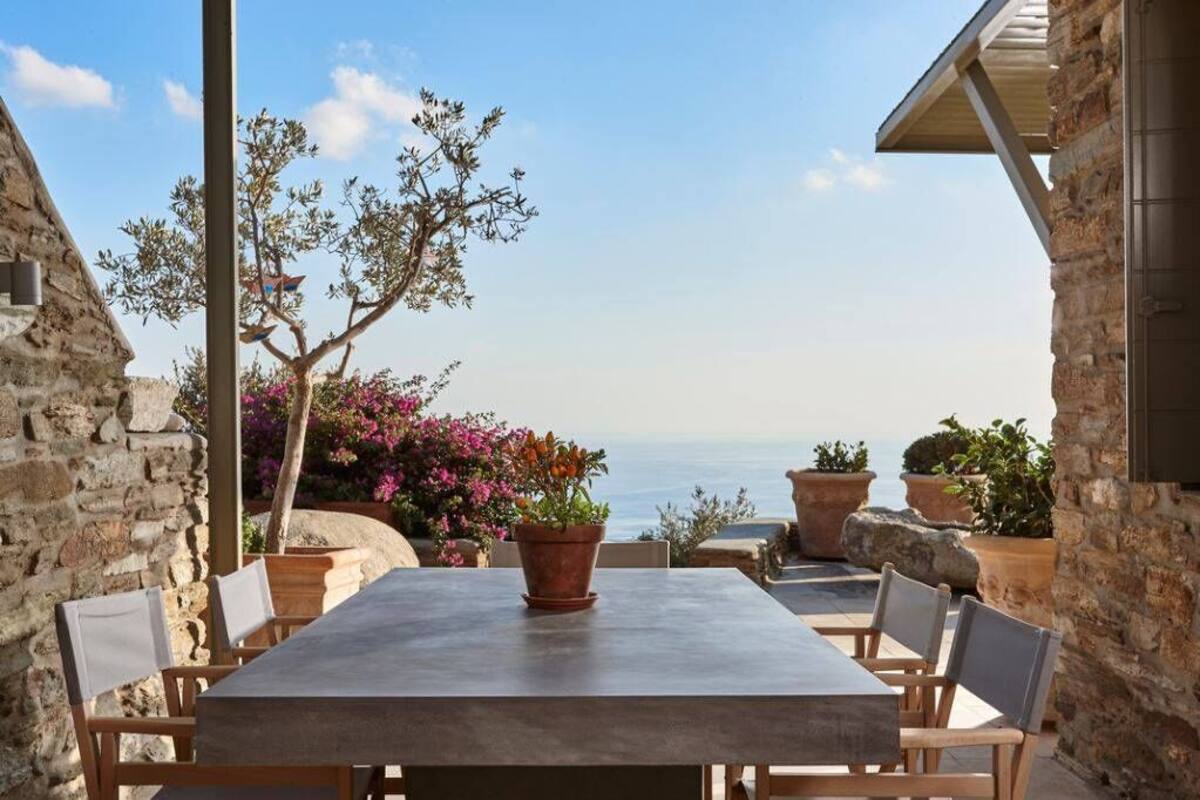 A stone building with a table and chairs, potted plants, and a view of the sea.